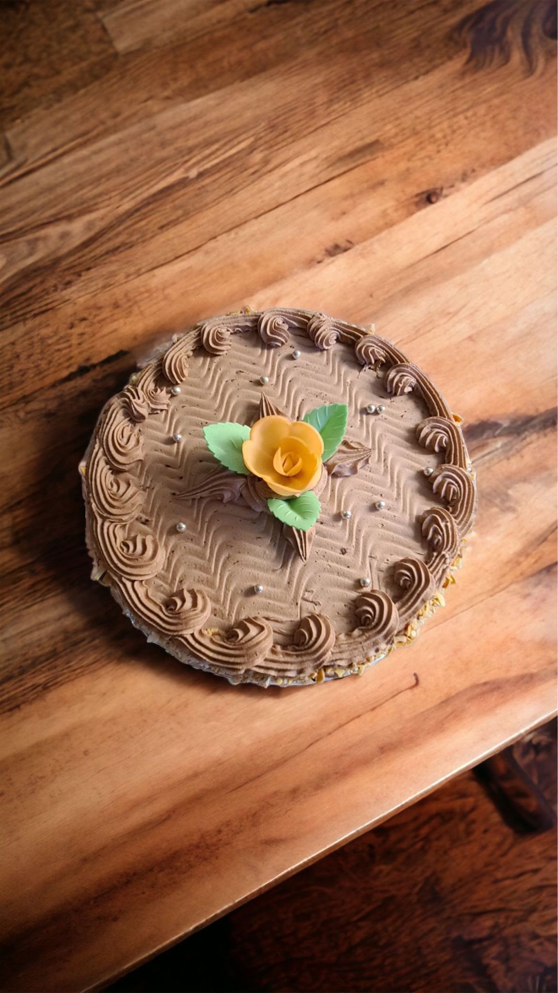 Gâteau glacé au chocolat avec une fleur jaune et des feuilles vertes sur une table en bois.
