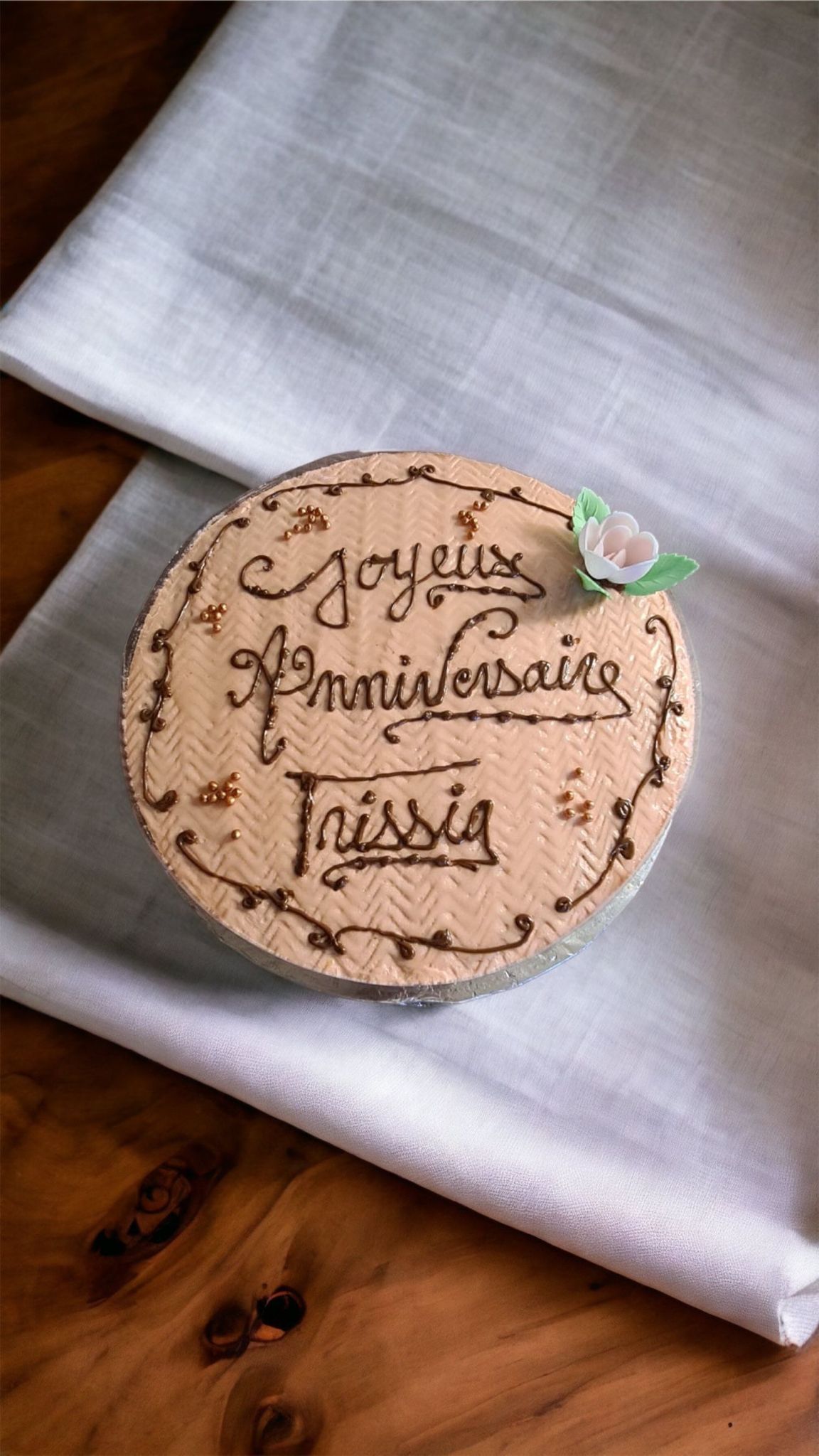 Gâteau d'anniversaire pour Trissia, rond, avec écriture et une fleur, sur une nappe blanche.