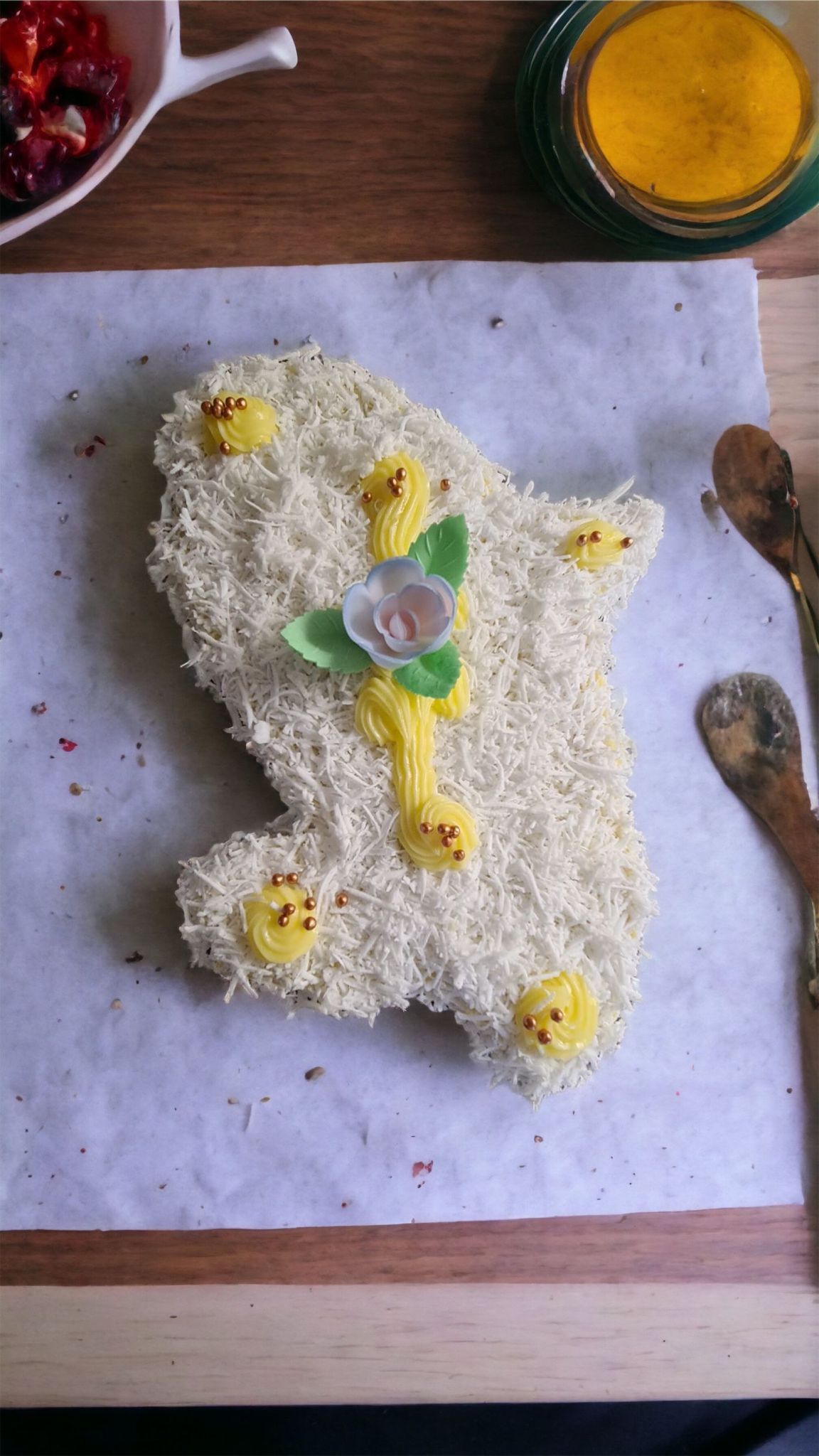 Gâteau décoré comme une mitaine, recouvert de vermicelles blancs, avec des décorations de poussins jaunes et une fleur.