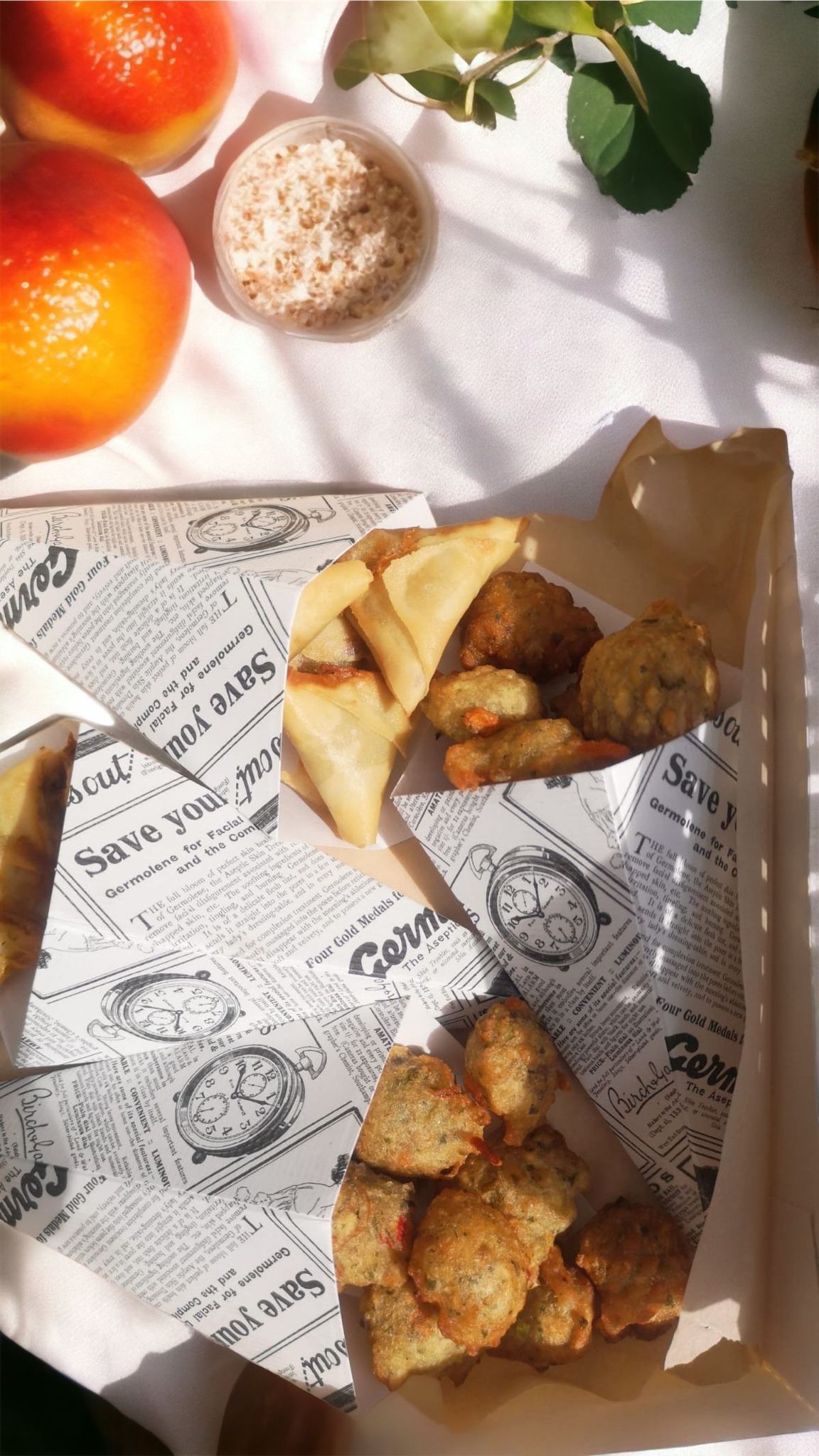 Frites dans des cornets en papier, à côté de fruits. Fond blanc, éclairage intense.