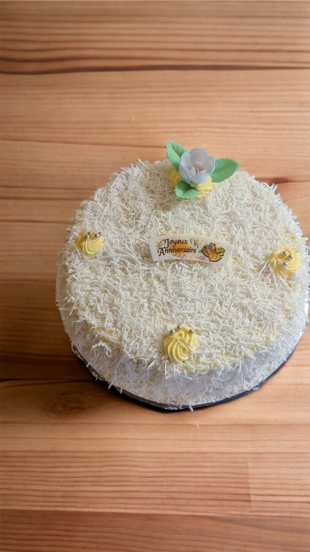 Gâteau glacé blanc avec des accents jaunes et des fleurs sur une table en bois.