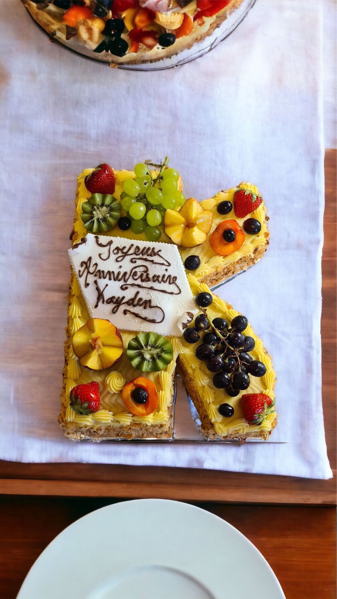 Gâteau avec la lettre « R » décoré de fruits, d'une assiette blanche et d'une tarte aux fruits.