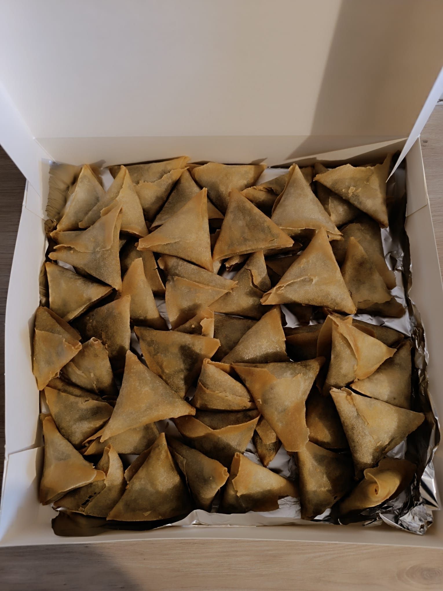 Boîte de nombreux samosas dorés, pâtisseries triangulaires, sur papier aluminium.