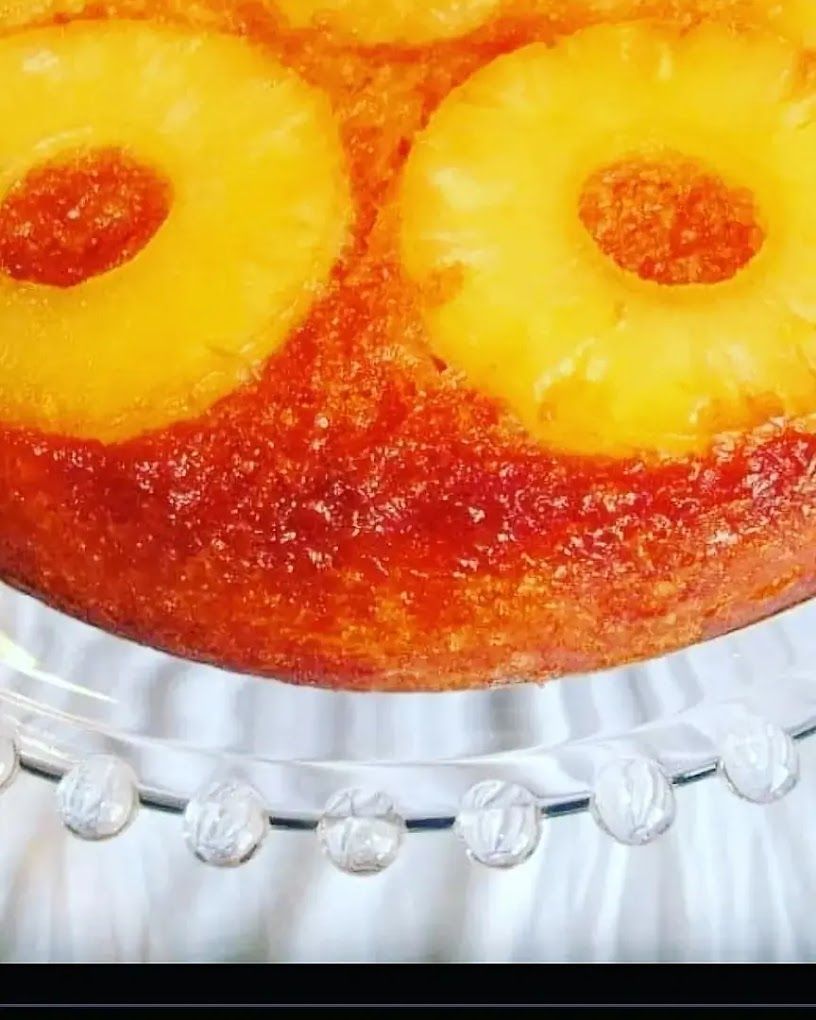 Gâteau à l'ananas renversé avec des anneaux d'ananas jaune vif, sur un support à gâteau en verre.