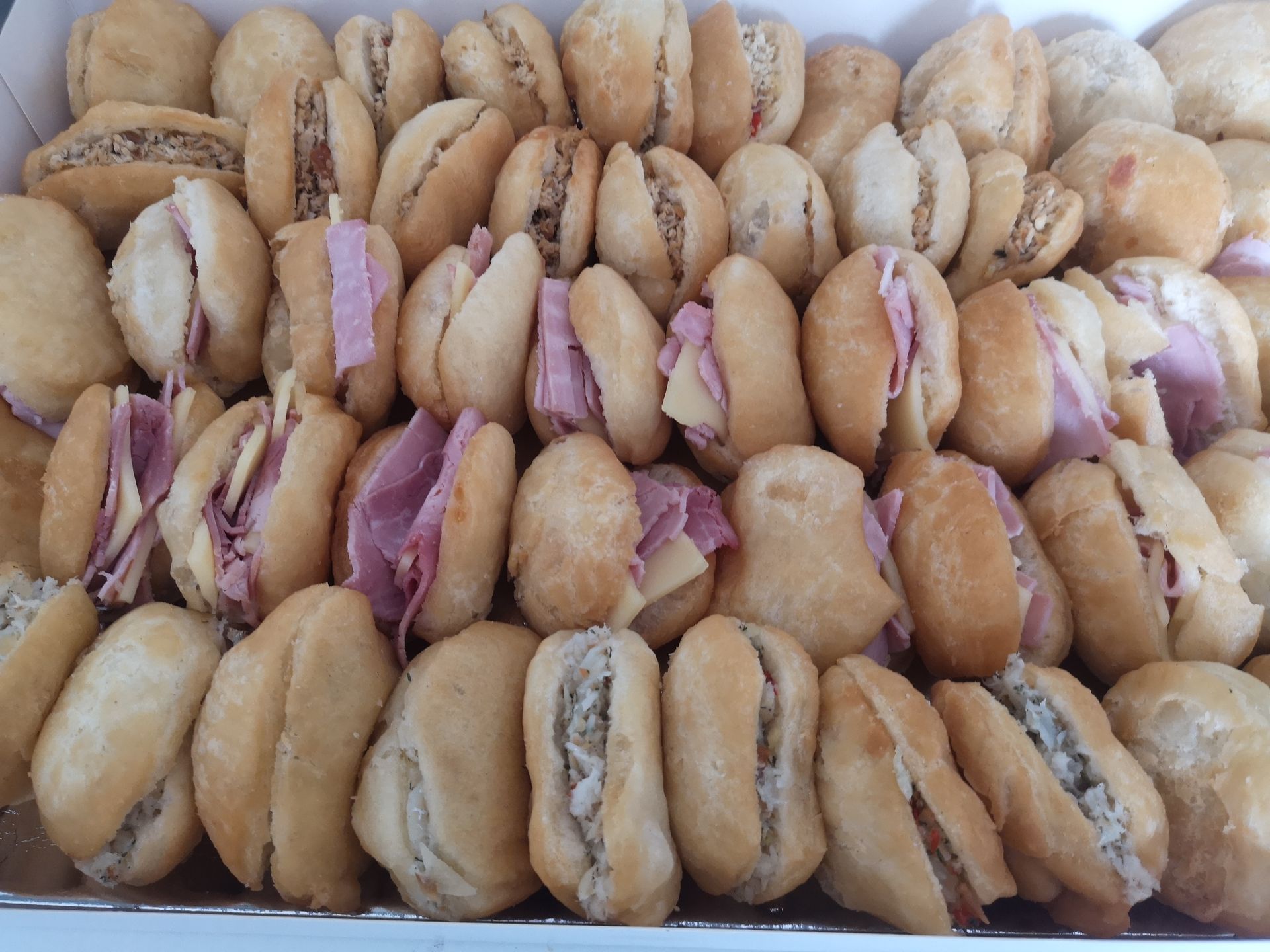 Boîte de mini sandwichs assortis, certains avec jambon et fromage, d'autres avec diverses garnitures.