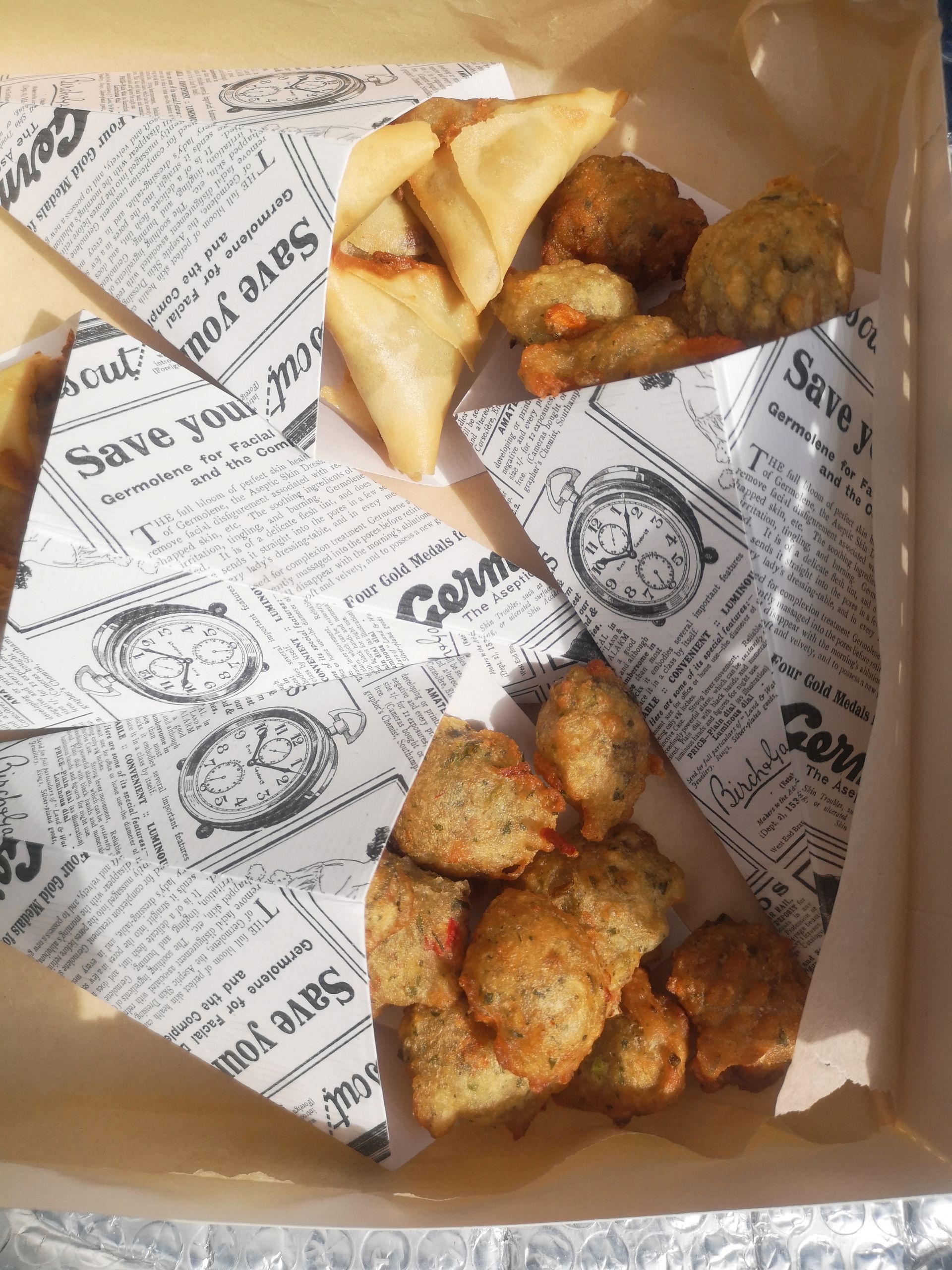 Boîte de collations frites assorties, comprenant des samosas et des beignets, dans des cornets en papier.