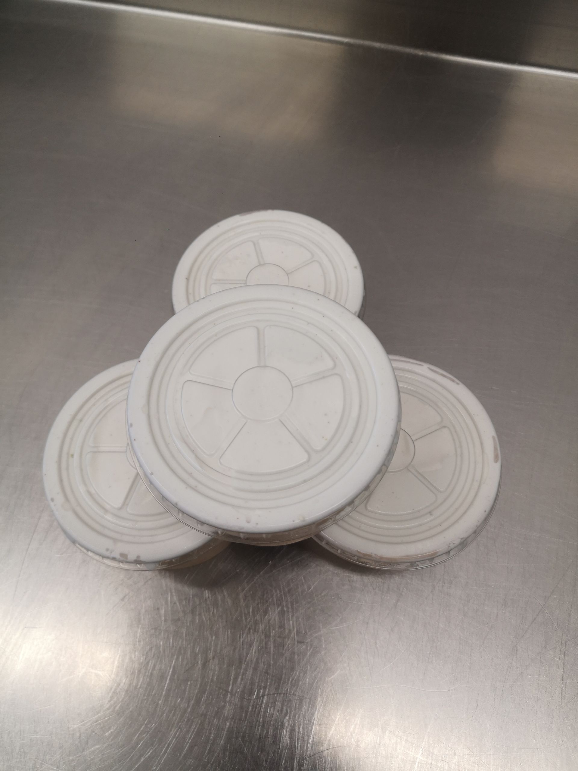 Quatre couvercles de boissons en plastique blanc empilés sur une surface en acier inoxydable.