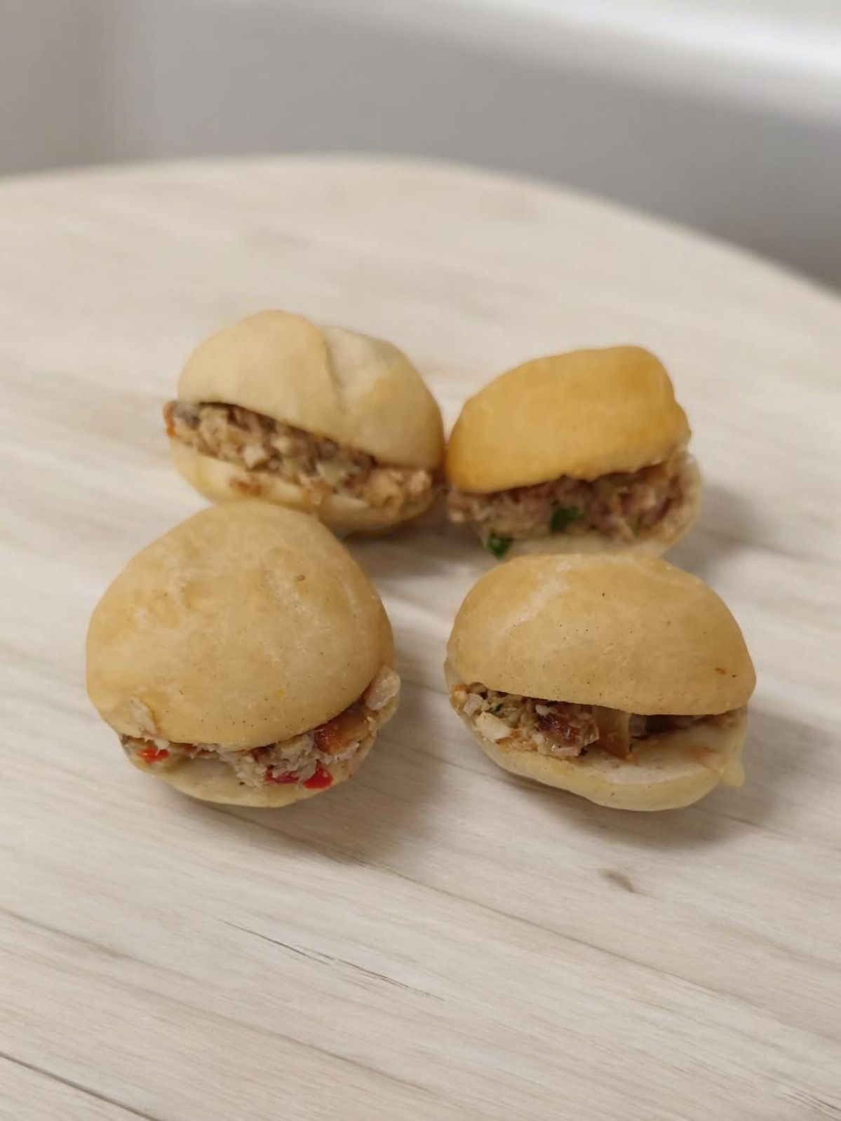 Quatre petits sandwichs sur une surface en bois clair, avec la garniture visible entre les petits pains ronds.