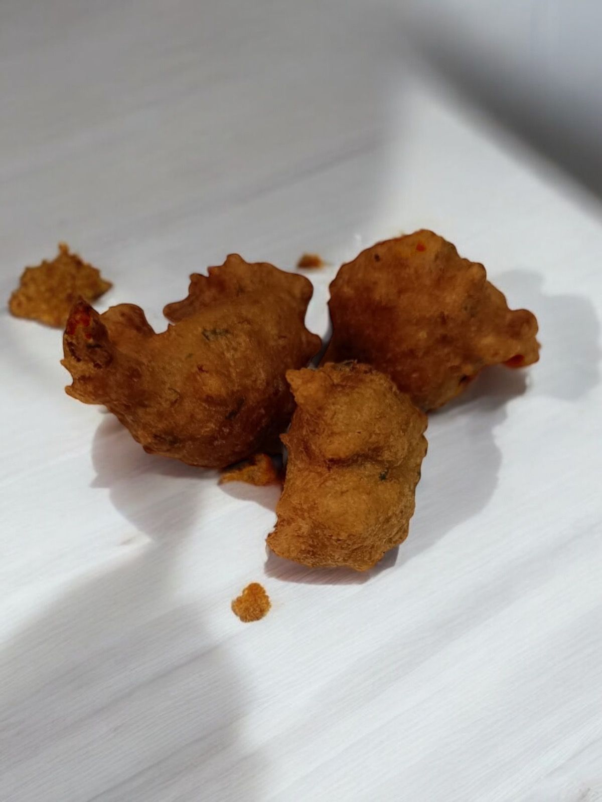 Beignets frits dorés sur du papier blanc, croustillants et de forme irrégulière.