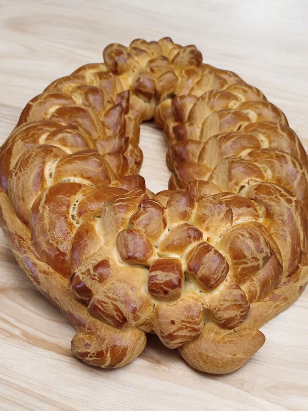 Pain doré tressé de forme ovale, posé sur un plateau en bois clair.