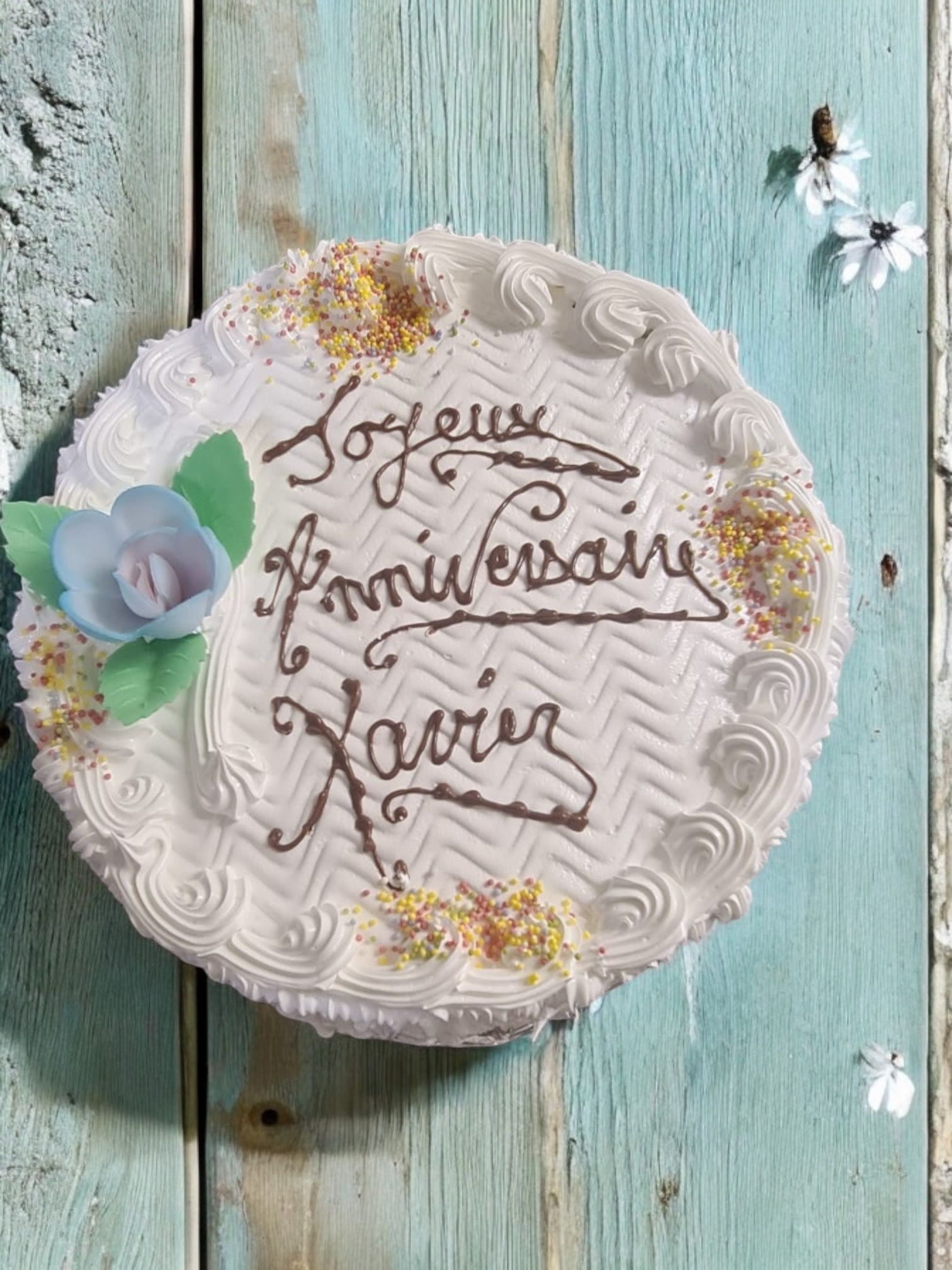Gâteau avec l'inscription « Joyeux Anniversaire Xavier » écrite en glaçage; décoré de vermicelles et d'une fleur.