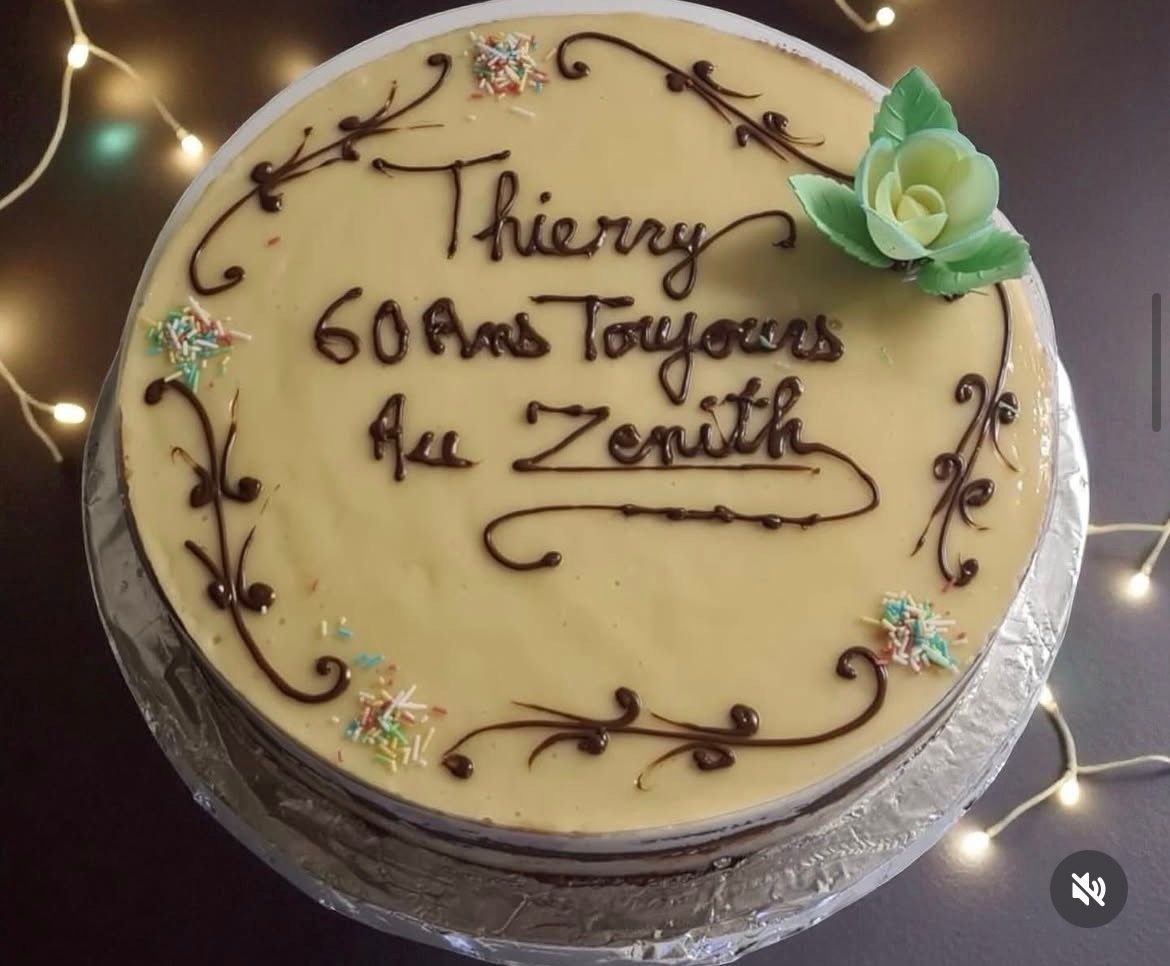 Gâteau rond à la crème avec inscription en chocolat « Thierry 60 ans Toujours Au Zenith » et décoration en fleur de sucre verte
