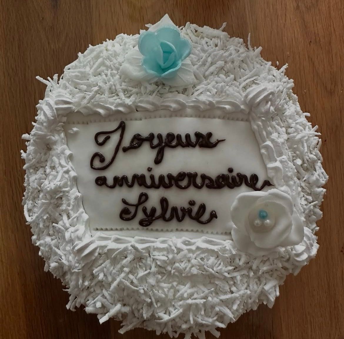 Gâteau d'anniversaire rond blanc avec inscription française et décorations florales turquoise et blanches