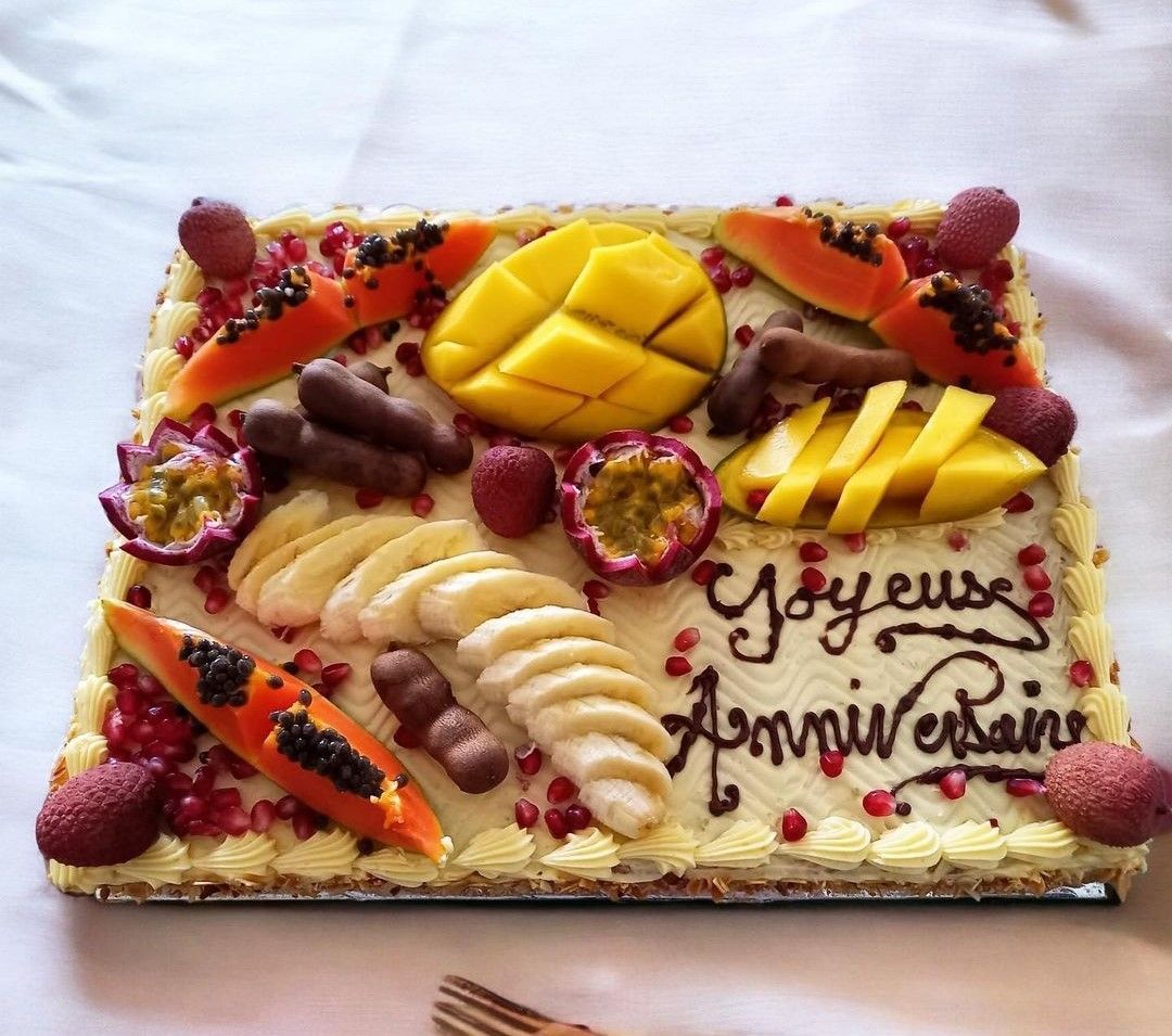 Gâteau d'anniversaire rectangulaire avec fruits tropicaux, glaçage et texte français.
