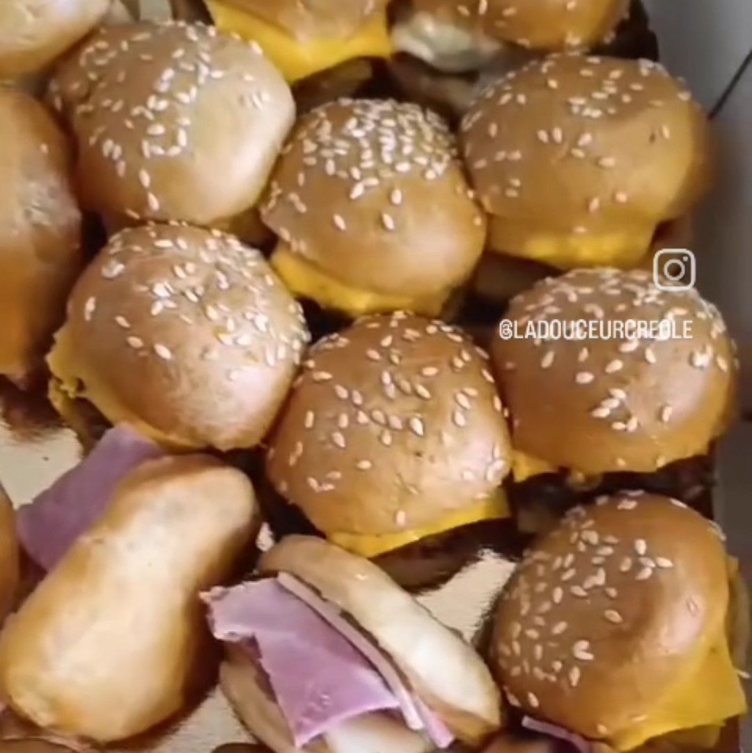 Mini cheeseburgers et sandwichs au jambon dans une boîte, avec des pains aux graines de sésame.