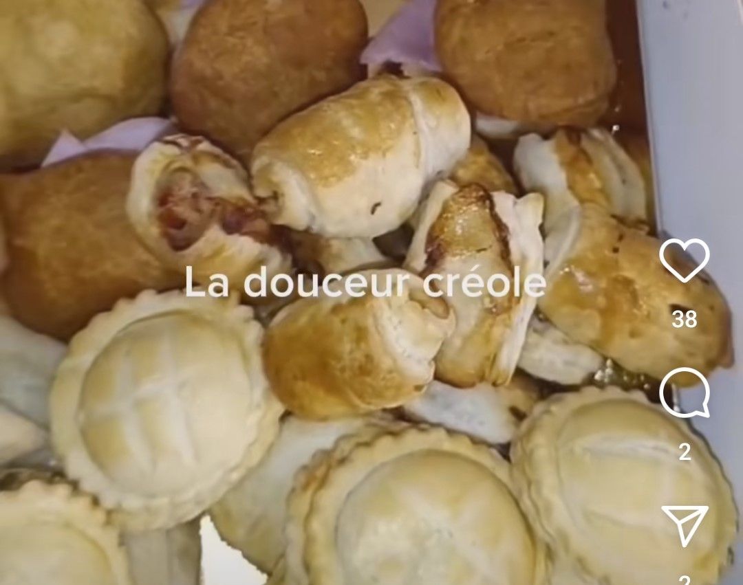 Assortiment de pâtisseries créoles cuites au four, dont des tartes salées et des petits pains, dans une boîte.