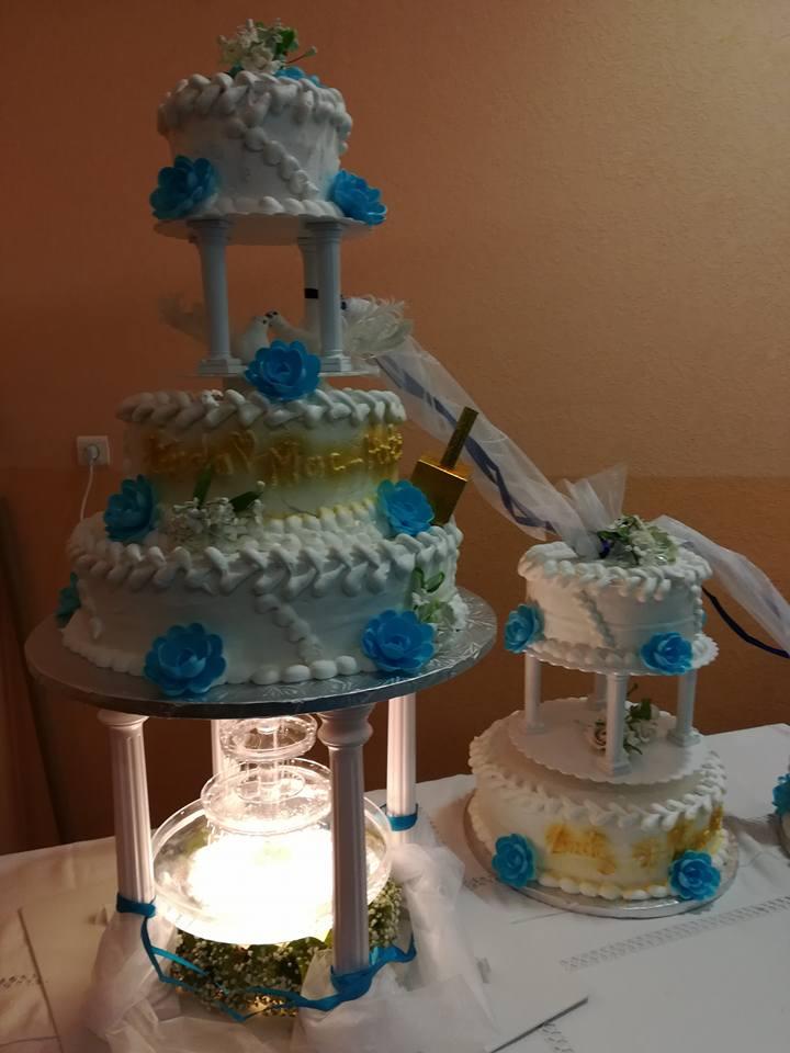 Gâteau à trois étages avec des fleurs bleues, sur une base de fontaine, à côté d'un gâteau plus petit et similaire, posé sur une table.