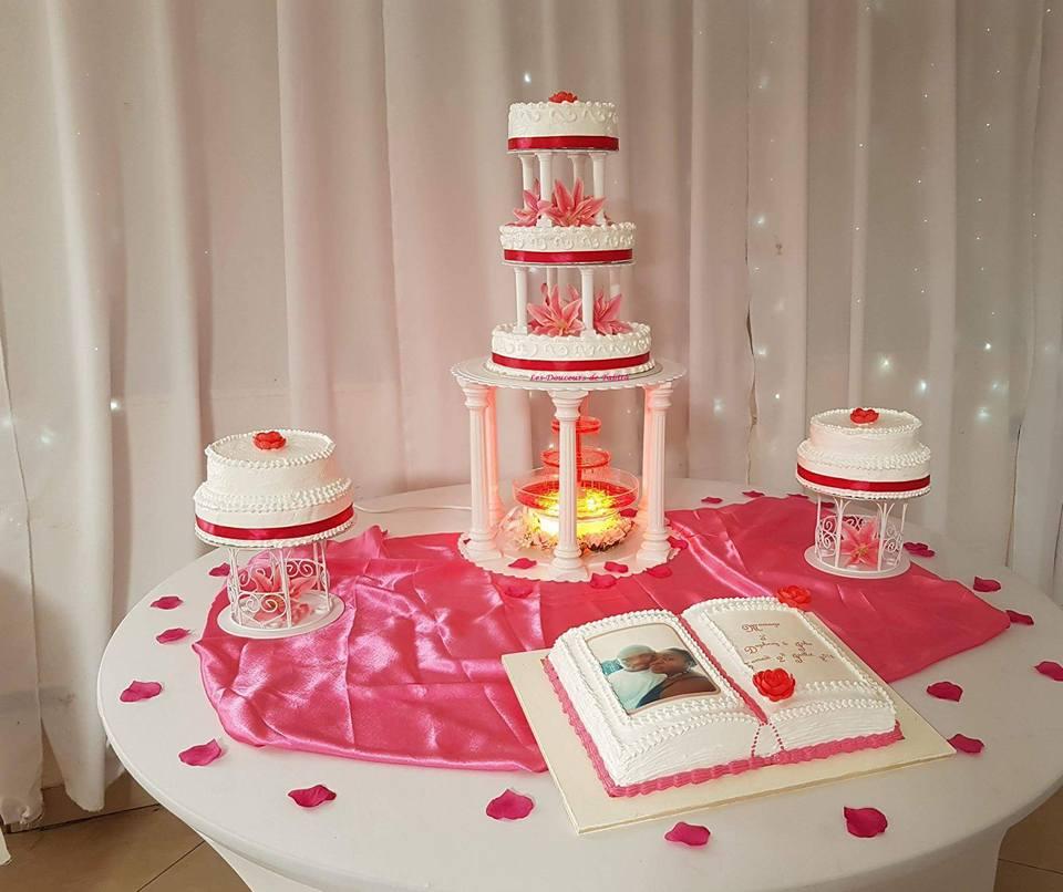 Présentation du gâteau de mariage : un gâteau à plusieurs étages, des gâteaux plus petits et un gâteau en forme de livre ouvert sur une table avec des accents et des pétales roses.
