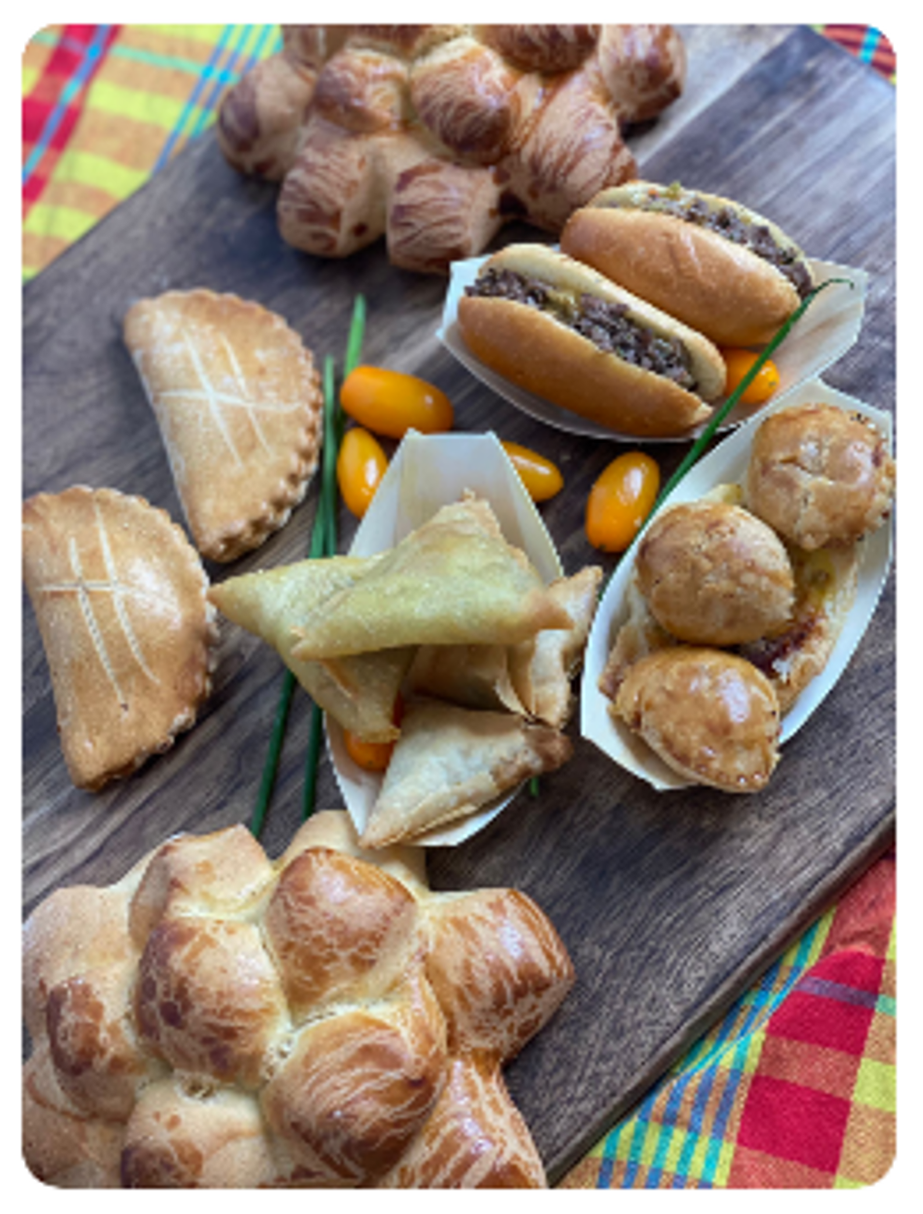 Planche en bois avec assortiment de pâtisseries : pain, mini-tartes, samosas, mini hot-dogs et tomates.