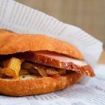 Sandwich avec jambon, oignons et fromage sur un pain rond, enveloppé dans du papier.