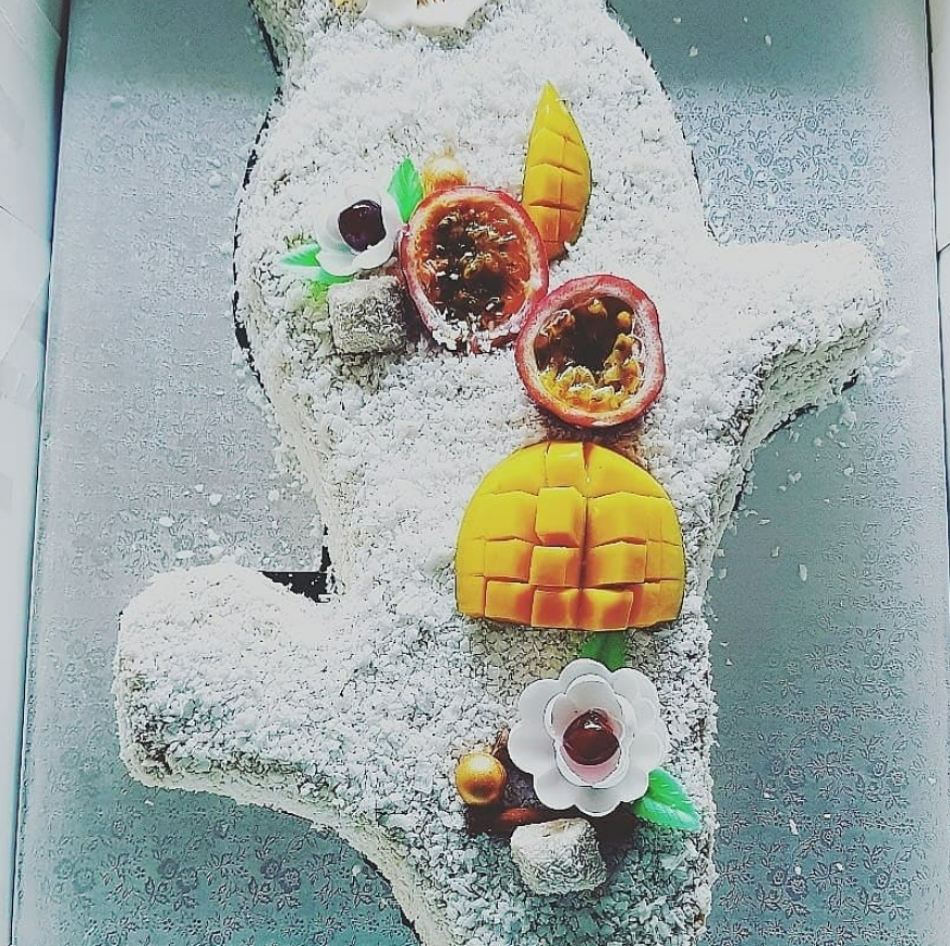 Gâteau en forme de cactus recouvert de flocons de noix de coco, décoré de fruits de la passion, de mangue et de fleurs.