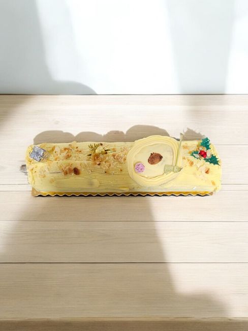 Bûche de Noël avec glaçage à la crème et décorations florales sur un support en bois.