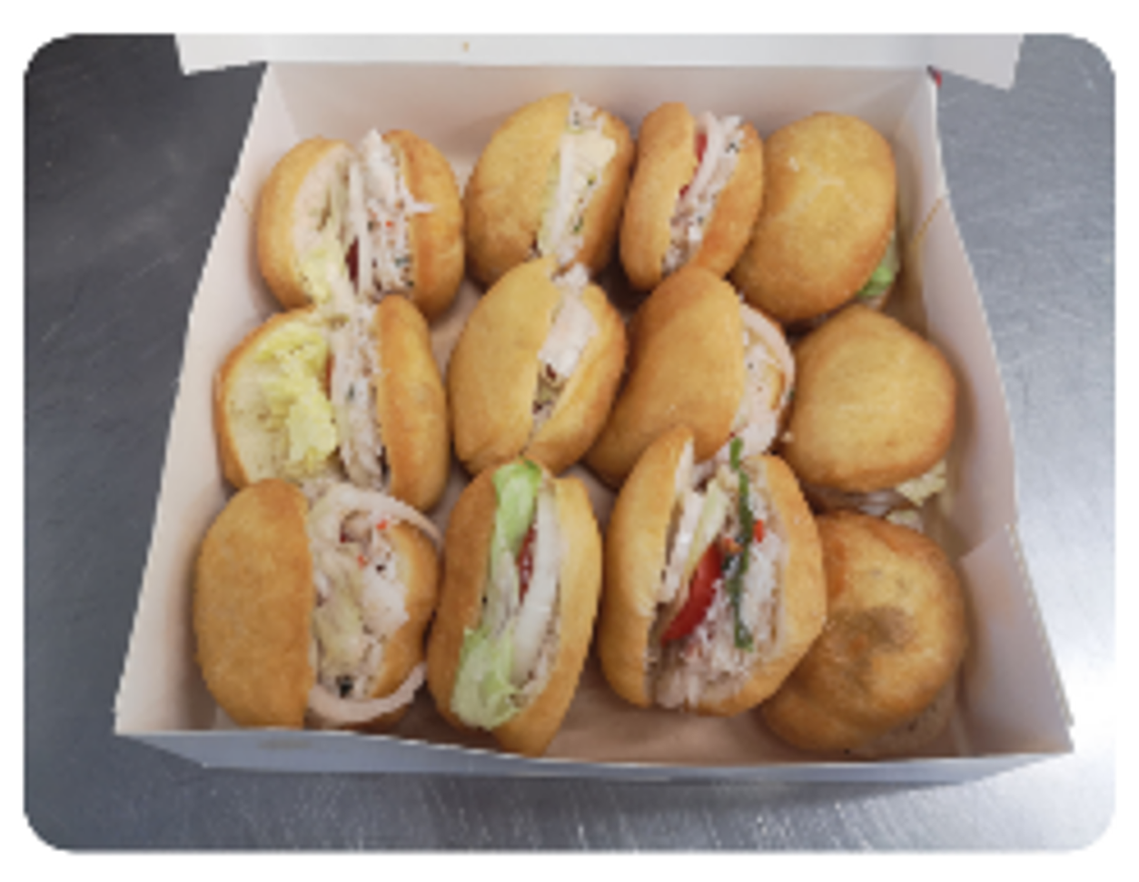 Boîte de mini sandwichs : petits pains dorés garnis de garniture blanche, de laitue et de tomates rouges.