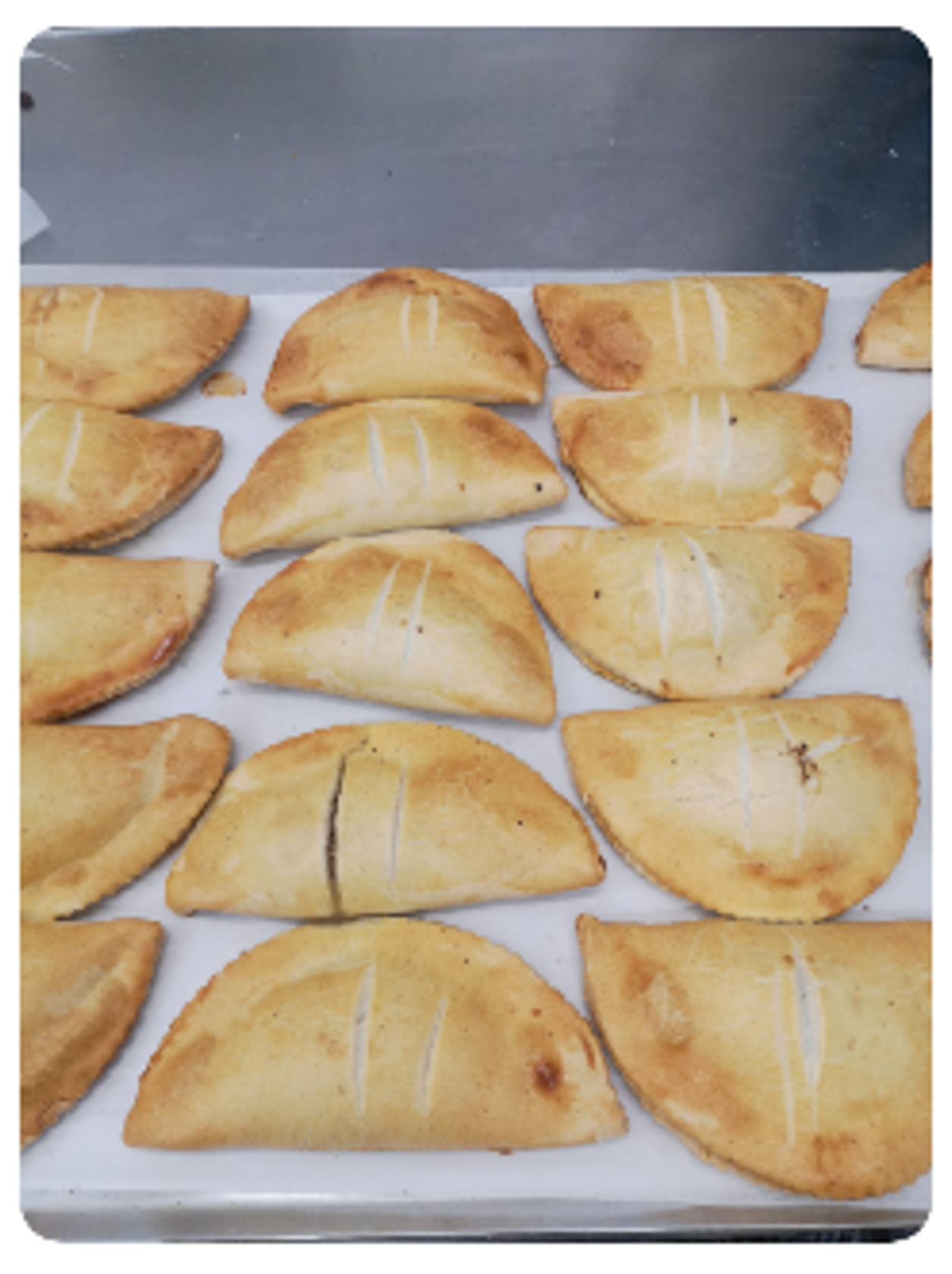 Pâtisseries dorées et cuites sur une plaque blanche, disposées en rangées sur une table.