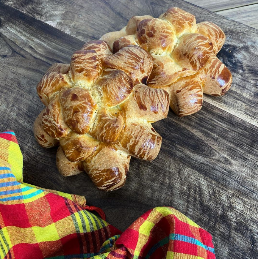 Pain brioché doré et brillant sur une surface en bois, à côté d'un tissu à carreaux coloré.