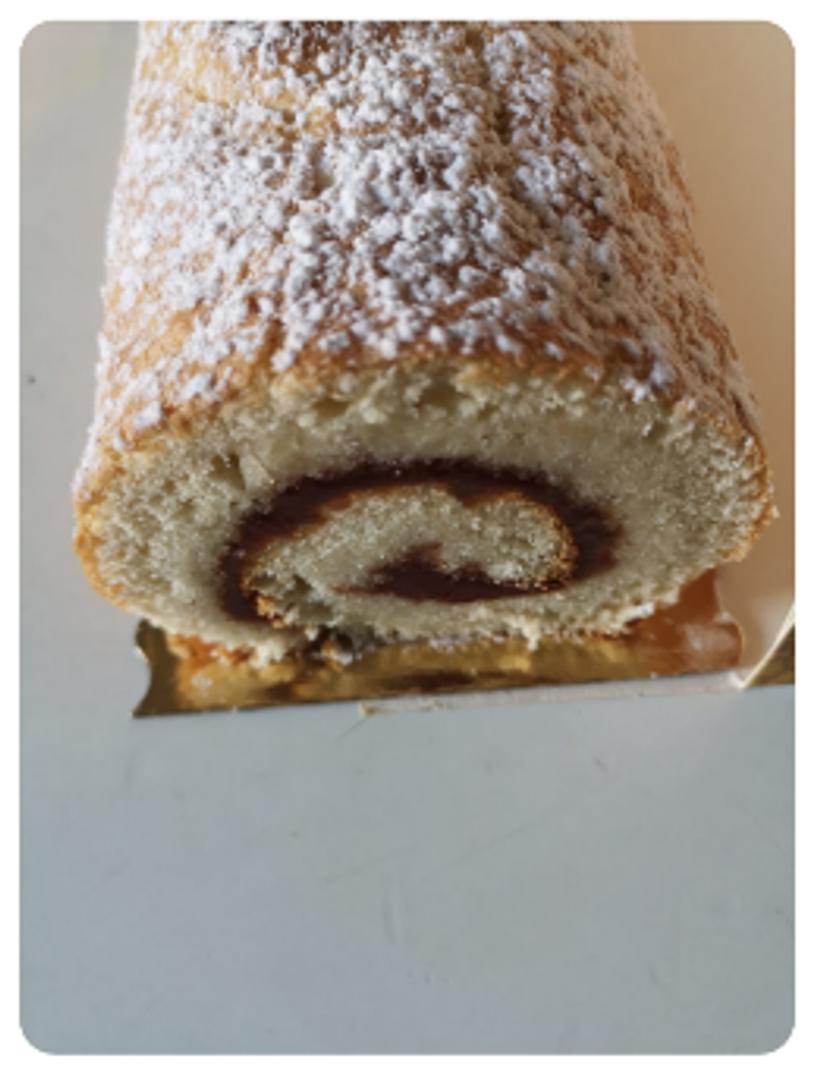 Gâteau roulé saupoudré de sucre glace, fourré de confiture noire.