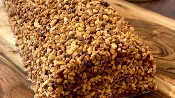 Gâteau recouvert de noix concassées sur une planche en bois.