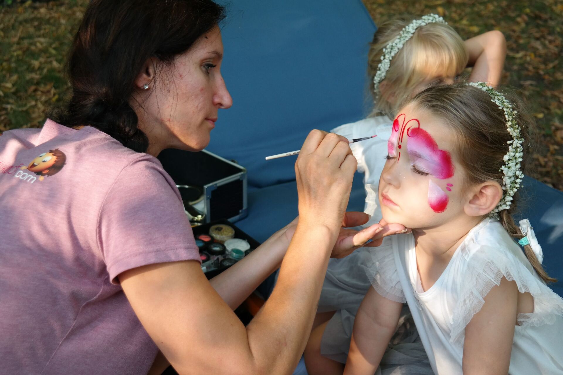 Eine Frau bemalt das Gesicht eines kleinen Mädchens mit einem Schmetterlingsmuster.