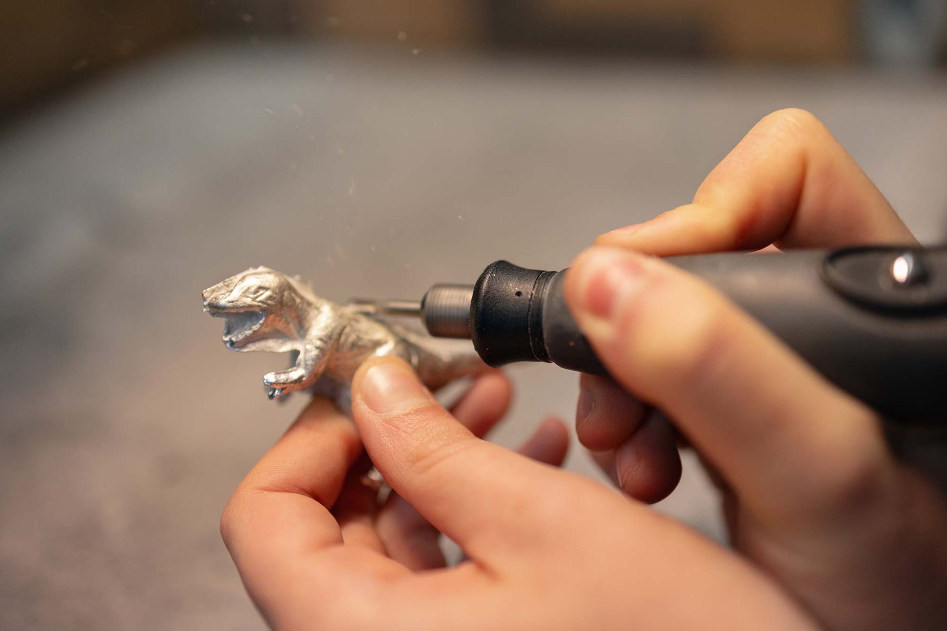 Eine Person poliert mit einer Maschine einen Spielzeugdinosaurier.
