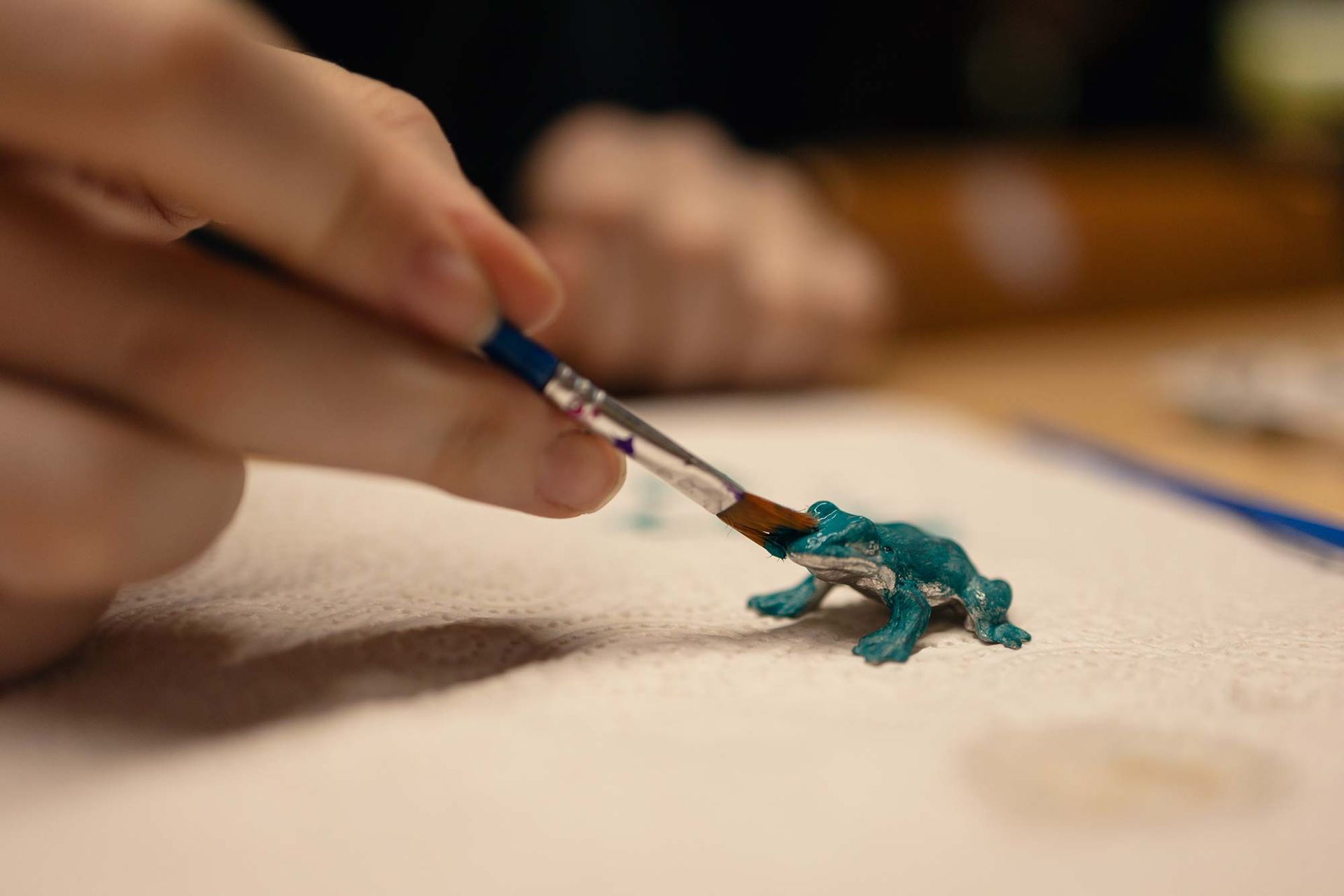 Eine Person bemalt einen Spielzeugfrosch mit einem Pinsel.