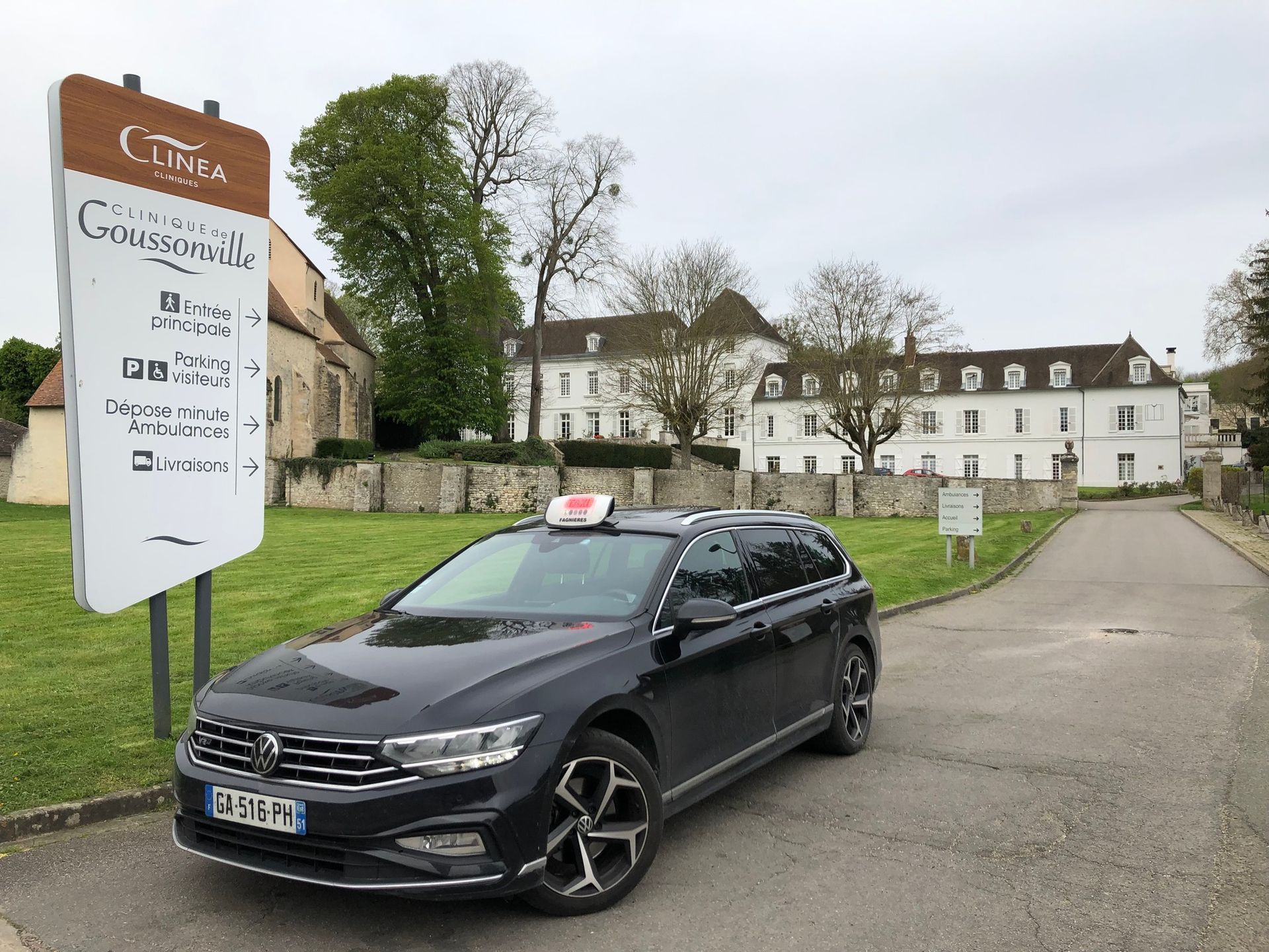 Taxi noir stationné devant un bâtiment blanc sous un ciel nuageux.