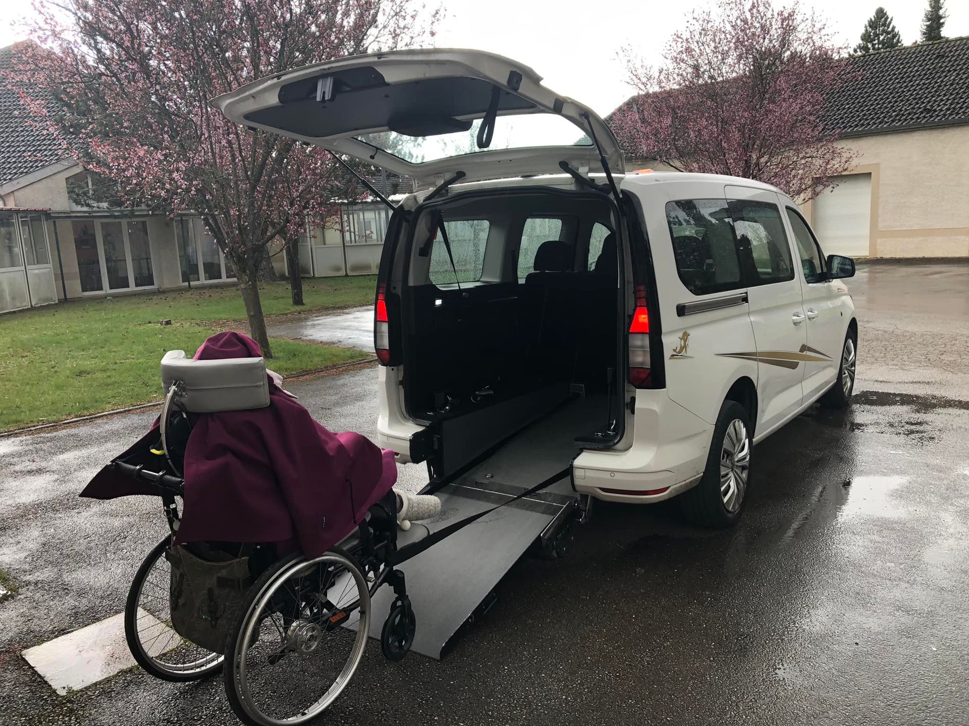 Une personne en fauteuil roulant entre dans un taxi  blanc par une rampe déployée.