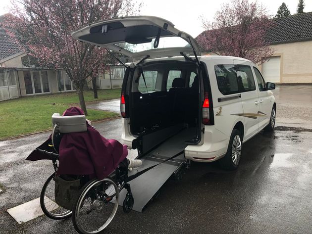 Une personne en fauteuil roulant entre dans un taxi blanc par une rampe déployée.