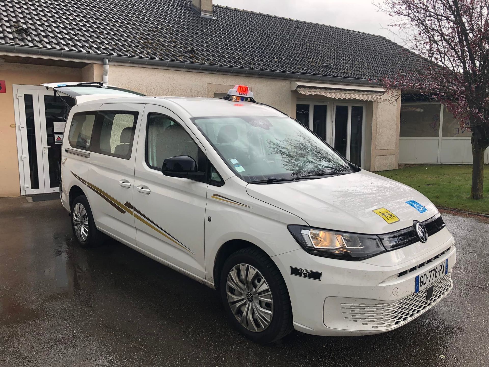 Un taxi PMR blanc avec des autocollants jaunes et noirs est garé devant un bâtiment.