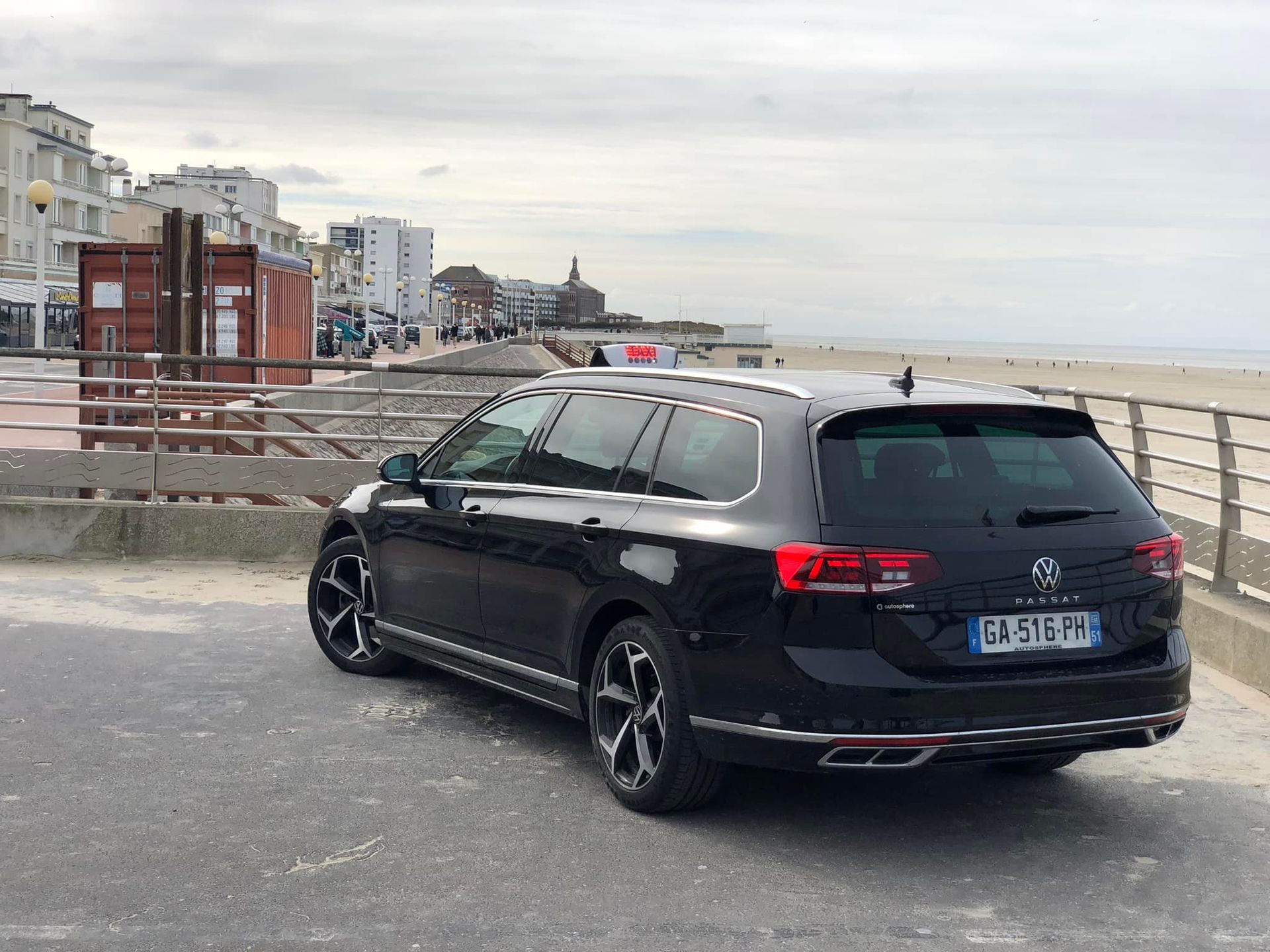 Un taxi break noir est garé sur une promenade en bord de mer. 