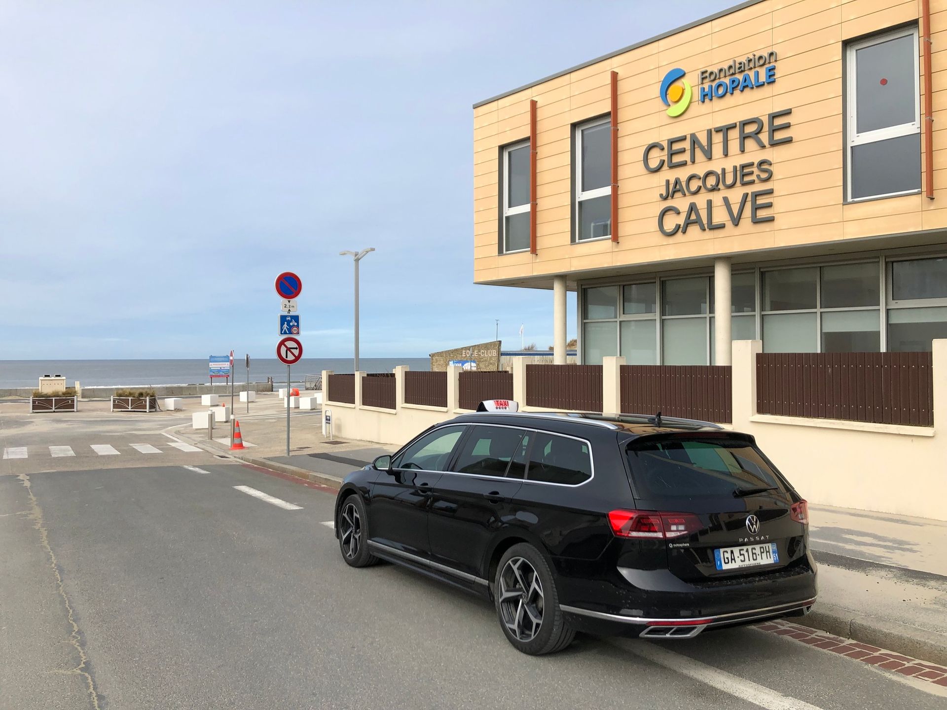 Taxi noir garé près du centre Jacques Calvé en bord de mer.