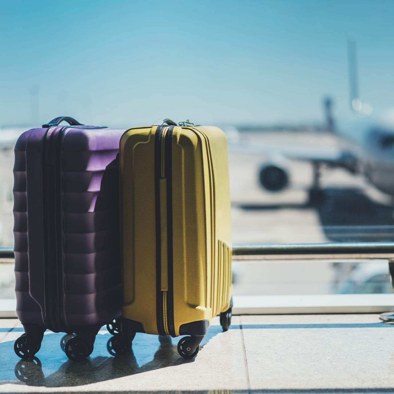 Des valises violettes et jaunes près d'une fenêtre donnant sur une piste d'aéroport.
