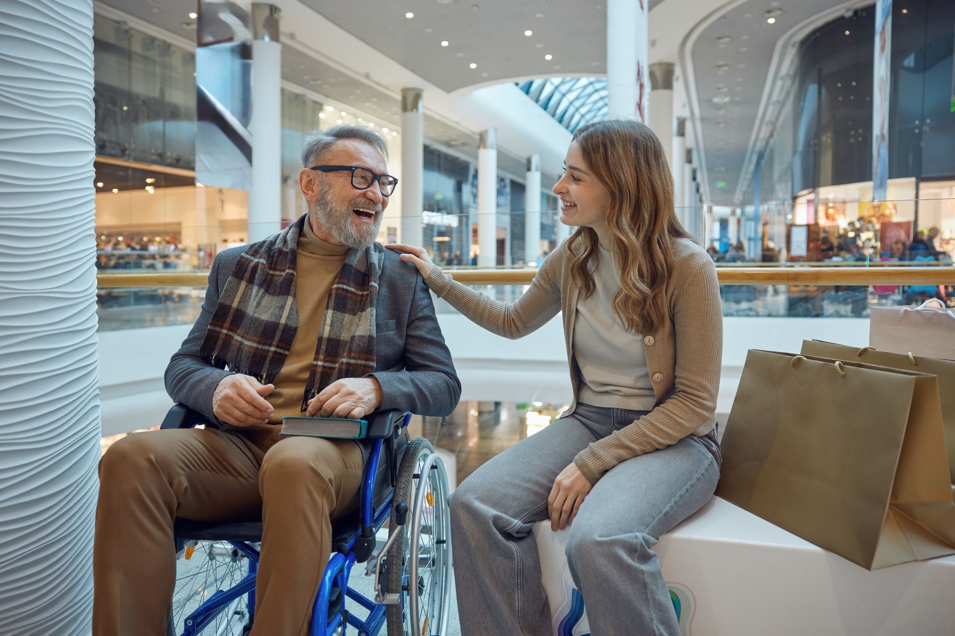 Un homme en fauteuil roulant sourit à une femme qui pose la main sur son épaule dans un centre commercial.