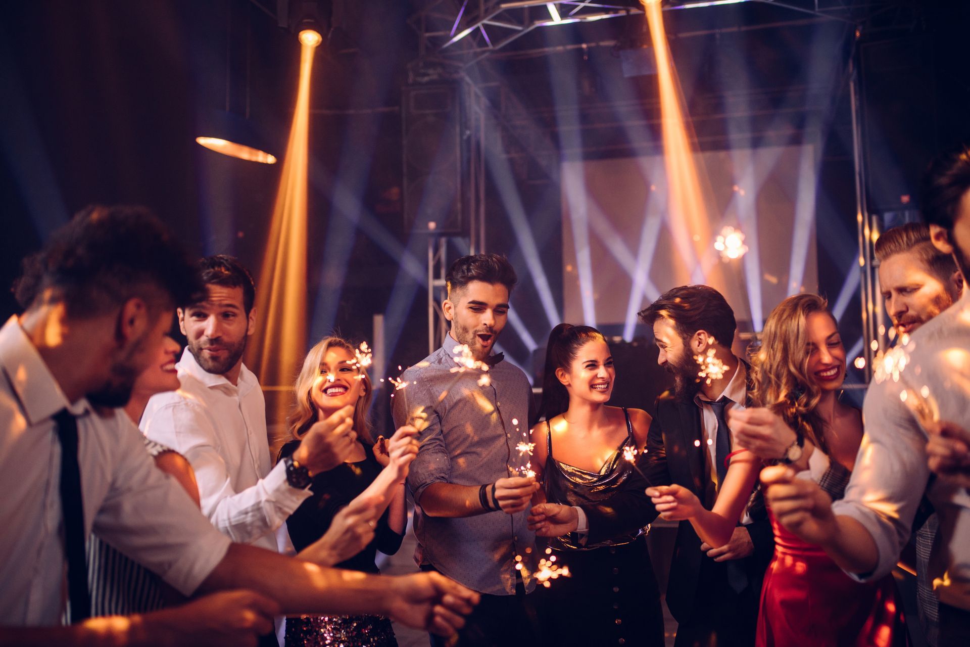 Des personnes font la fête dans une boîte de nuit, illuminée par des projecteurs.