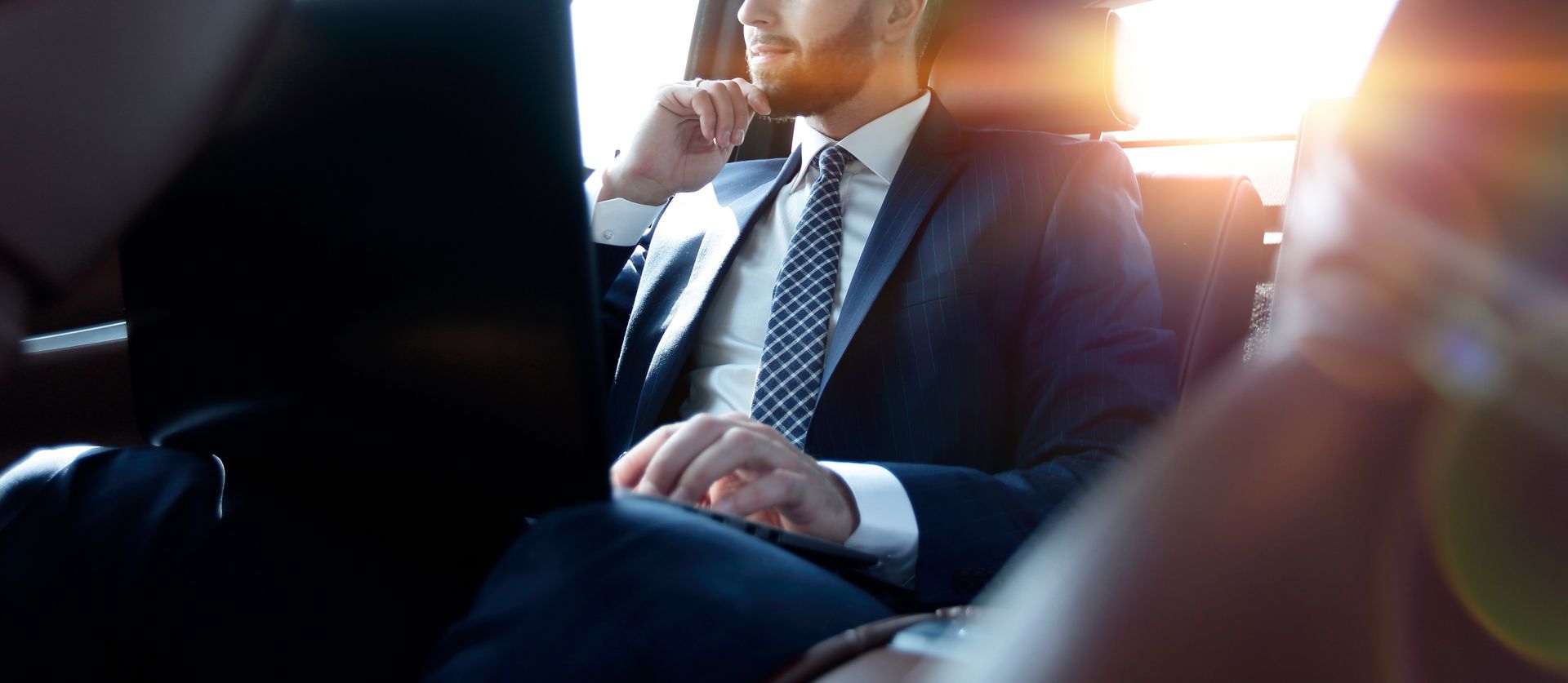 Un homme en costume est assis dans une voiture, regardant par la fenêtre.