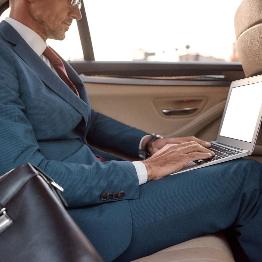 Un homme en costume bleu travaille sur son ordinateur portable dans sa voiture.