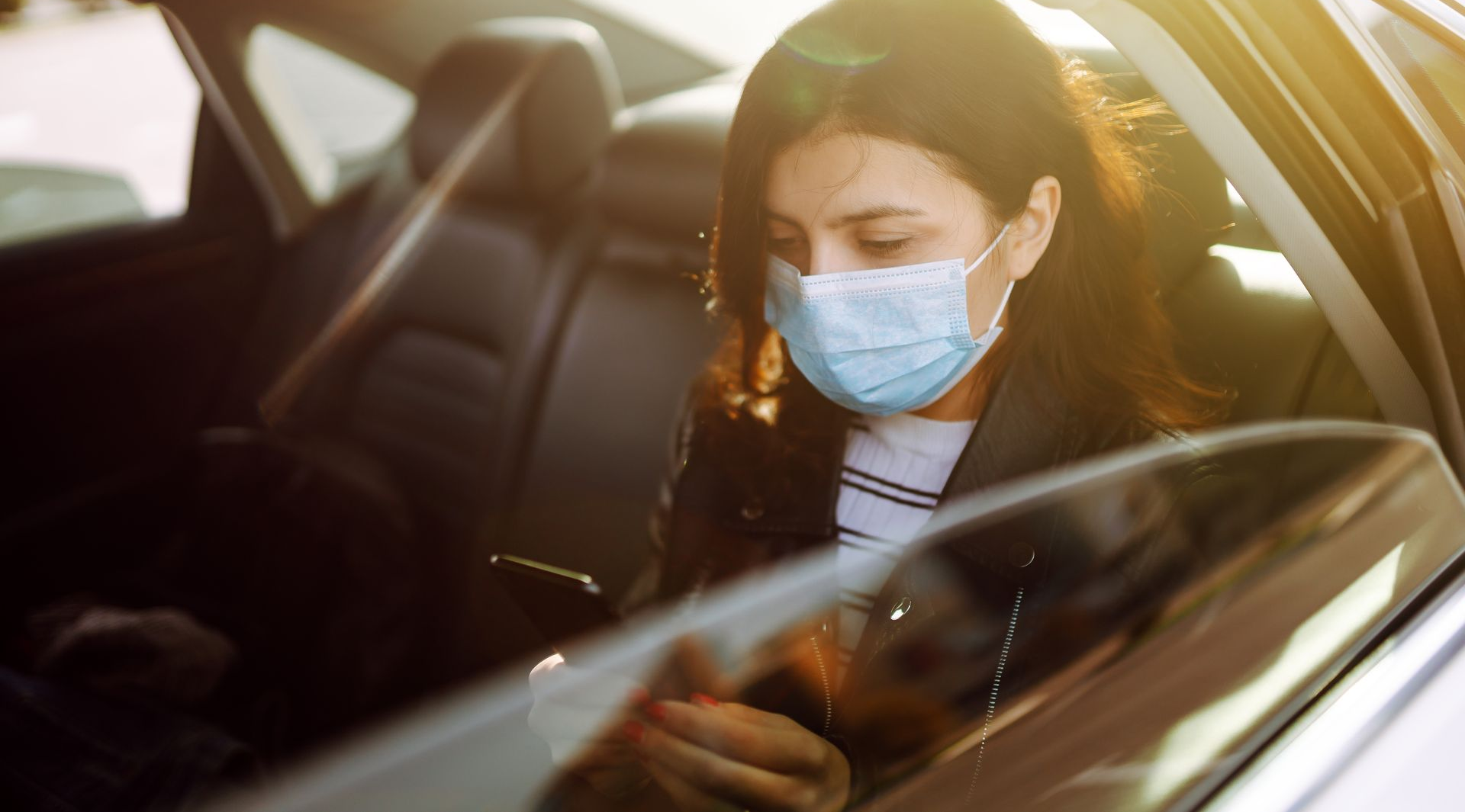 Femme portant un masque dans une voiture, regardant son téléphone.