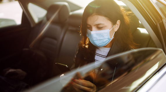 Femme portant un masque dans une voiture, regardant son téléphone.