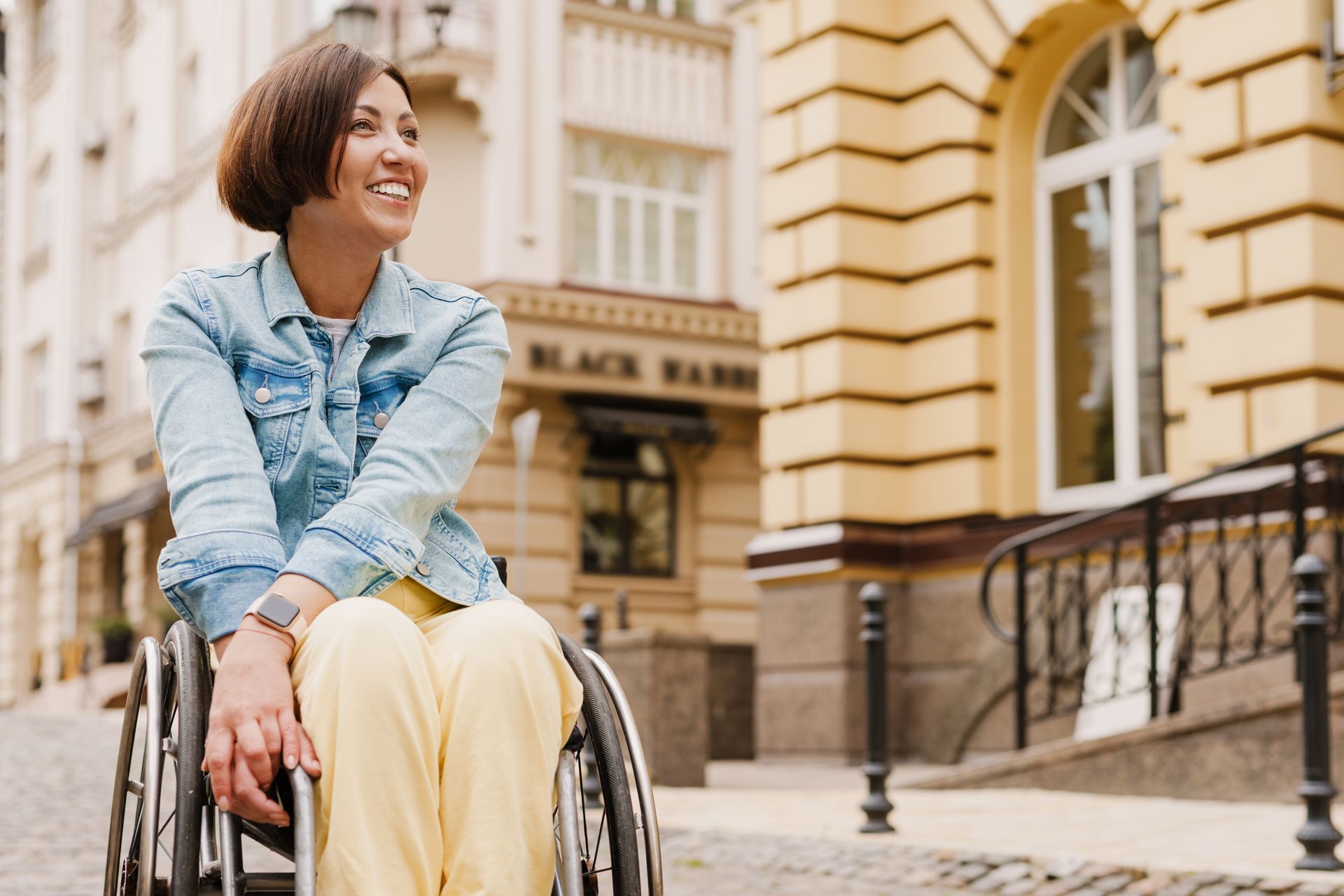 Une femme souriante en fauteuil roulant dans une rue.