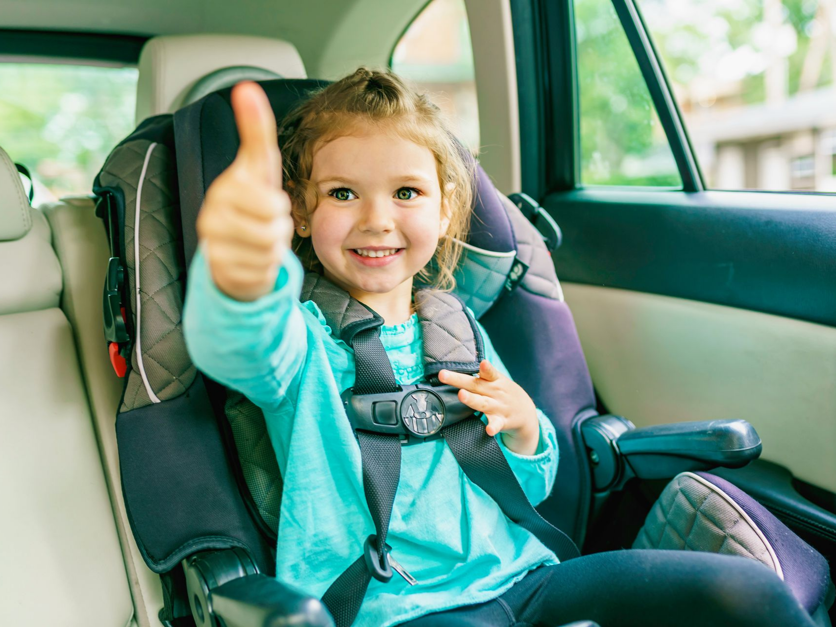 Enfant installé dans un siège auto, pouce levé.