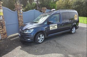 Un taxi van noir est garé devant un hôtel au toit marron.